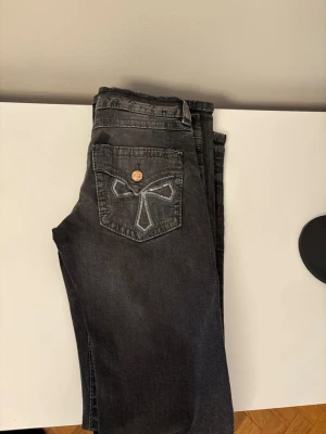 Grå jeans med broderad bakficka - Snygga grå jeans med en unik broderad detalj på bakfickan. Jeansen har knapp och dragkedja framtill samt slitningar för en cool look. 