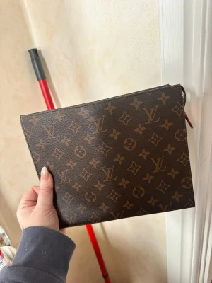 monogram kuvertväska - Snygg kuvertväska  i klassiskt brunt monogrammönster med guldiga detaljer. Dragkedjan är trasig har lossnat på ena sidan går säkert att fixa