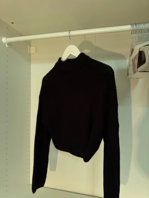 Svart stickad tröja från Divided - Säljer en svart stickad tröja från Divided med hög hals och långa ärmar. Tröjan har en croppad passform och är stickad i mjukt material. Perfekt för dig som gillar en enkel men trendig look.