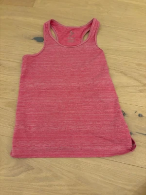 Rosa linnetopp från 157.FUNK - Säljer ett sportigt rosa linnetopp från 157.FUNK. Toppen är ärmlös med brottarrygg och har en melerad look. Tillverkad i mjuk och stretchig polyester och spandex, perfekt för träning eller chill dagar.