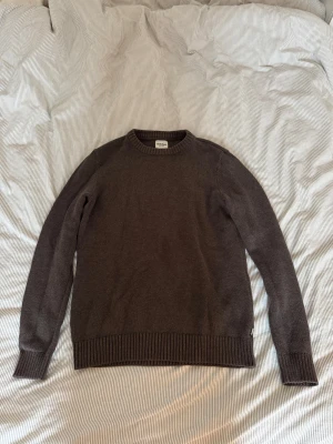 Brun stickad tröja från Dobber - Snygg brun stickad tröja från Dobber med rund hals och ribbade muddar vid ärmslut och nederkant. Perfekt för dig som gillar enkel och stilren design. Materialet är mjukt och skönt, och tröjan har en normal passform med långa ärmar.