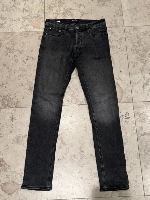 Svarta slim jeans från Jack & Jones - Svart/gråa jeans från Jack & Jones i modellen Slim/Glenn. Jeansen har en smal passform, klassisk femficksdesign och svarta sömmar. Materialet är stretchigt jeans och midjan är normal. Perfekt för dig som gillar en clean och modern look. Knappt använda. Storleken är 28/32. Nypris 799kr, mitt pris 200kr!