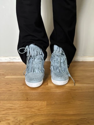 Ljusblå mocka boots med fransar - Unika ljusblå boots i mocka med snörning och coola fransdetaljer runt hela skon. Skorna har en platt vit sula en kilklack.