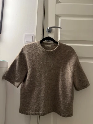 Beige stickad t-shirt i ullblandning - Kortärmad stickad tröja i mjuk beige ullblandning med rund hals och ribbade kanter. Enkel och stilren design som passar perfekt till lager på lager eller för en chill look. Oversized passform för extra komfort.