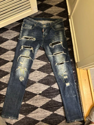 Blå slitna skinny jeans med hål - Säljer ett par blå skinny jeans med stora slitningar och hål framtill samt färgstänk i gult och vitt. Jeansen har klassisk femficksmodell och är tillverkade i denim. Perfekta för dig som gillar en edgy och trendig stil.