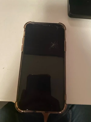 iPhone med svart framsida och skal - Säljer en iPhone med svart framsida och genomskinligt skal. Telefonen har en klassisk rektangulär form och är tillverkad i glas och metall. Perfekt för dig som gillar Apple och vill ha en stilren mobil. Sprickorna i framsida skärm gör ingen skillnad till mobilens funktion. Face ID funkar tyvärr inte och batterikapaciteten är på 71% men det går att byta om man skulle vela det. Låda till mobil kommer med.