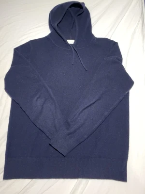 Mörkblå Kashmir hoodie - Snygg mörkblå hoodie med huva och dragsko. Tillverkad i kashmir, perfekt för en avslappnad stil. Klassisk passform med ribbade muddar vid ärmslut och nederkant. Enkel och stilren design utan tryck eller logga.