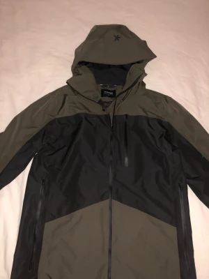 Jacka  Everest  - Säljer en snygg vindjacka från Everest i svart och olivgrönt. Jackan har huva, hel dragkedja och två sidofickor med dragkedja. Reflextape på huvan baktill. Perfekt för blåsiga dagar och outdoor-häng. Varm och stilig