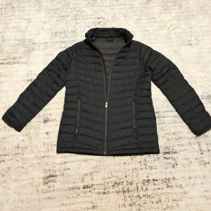 Dunjacka från Ralph Lauren - Snygg svart dunjacka från Ralph Lauren dragkedja framtill. Jackan har två praktiska fickor med dragkedja och en klassisk krage. Perfekt för kyliga dagar och enkel att matcha med olika outfits.