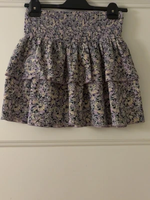 Ljuslila blommig volangkjol - Supersöt kort volangkjol i ljuslila med blommigt mönster. Kjolen har smock i midjan och dubbla volanger som ger en härlig och luftig känsla. Bara att fråga ifall du undrar något eller vill ha fler bilder! Pris kan diskuteras💞