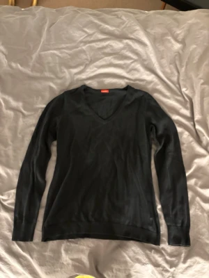 Svart V-ringad tröja - En stilren svart tröja med V-ringning och långa ärmar. Perfekt för lager-på-lager och enkel att matcha med olika outfits. Tröjan har ribbade muddar vid ärmslut och nederkant.