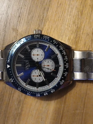 Regal kronografklocka i stål - Snygg kronografklocka från Regal med blå urtavla, silverfärgade detaljer och tachymeter på boetten. Klockan har tre subdials och ett robust armband i rostfritt stål. Perfekt accessoar för dig som gillar sportig och stilren design.