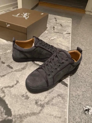 Gråa loubs utan spikar - Snygga grå sneakers från Christian Louboutin i mjuk mocka med rund tå och klassisk snörning. Skorna har diskreta sömdetaljer och en stilren design som passar perfekt till streetwear eller mer dressade outfits.