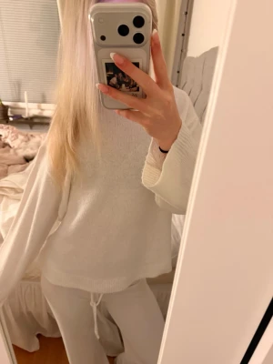 Vit stickad tröja - Mysig vit stickad tröja med rund hals och långa ärmar. Tröjan har en avslappnad passform och ribbade muddar vid ärmslut och nederkant. Perfekt för en chill och stilren look.