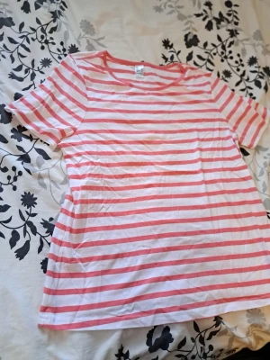 Randig T-shirt stl 44 – Klassisk marin stil - Säljes:  Snygg och bekväm kortärmad tröja i storlek 44. Vit med korallröda/rosa ränder. En perfekt basmodell som fungerar till det mesta! Storlek: 44 (Dam) Färg: Vit/Röd-randig Skick: Mycket gott skick   Skickas via posten & köpare står för frakten. Vid övriga frågor skicka gärna meddelande.  Titta gärna på mina andra annonser (har även en Michael Kors-topp ute & fin skinnkjol!) 