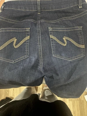 Mörkblå bootcut jeans från Nelly - Mörkblå jeans från Nelly med bootcut-modell och klassisk femficksdesign. Snygga kontrastsömmar och broderade bakfickor ger extra detaljer. Jeansen har normal passform och är tillverkade i stretchigt jeansmaterial.
