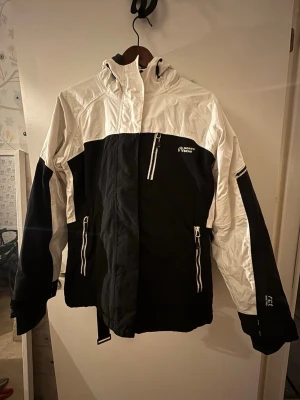 NorthBend skidjacka+byxor - Skidjacka+byxa i bra skick med hel dragkedja framtill. Jackan har flera fickor: 3 st fram varav ena är på bröstet, en på vä arm, två innerfickor, den ena har ett hål för tex hörlurar+dragkedja. Byxorna har tre fickor plus hängslen. Enda synliga slitaget är ett brännmärke på kanten av luvan (SE BILD) 