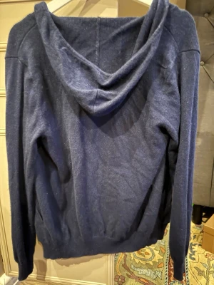 Mörkblå cashmere hoodie John Henric - Mysig mörkblå hoodie i 100% cashmere från John Henric. Tröjan har långa ärmar, huva och ribbade muddar vid ärmslut och nederkant. Perfekt för dig som vill ha något både stilrent och bekvämt i garderoben.