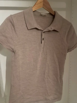 Beige pikétopp från John Henric - Snygg beige pikétopp från John Henric med klassisk krage och korta ärmar. Toppen har knappar framtill och är tillverkad i mjukt material som känns skönt mot huden. Perfekt för en stilren och avslappnad look. Passformen är slim, skriv om mer bilder eller annat