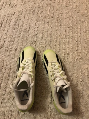 Adidas Crazyfast vita fotbollsskor - Snygga Adidas Crazyfast fotbollsskor i vitt med svarta detaljer och limegröna inslag. Skorna har snörning och är designade för fart på planen. Perfekta för dig som vill sticka ut med stil och prestanda.