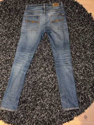 Blå jeans från Nudie - Säljer ett par blå  jeans från Nudie Jeans med slitningar och råa kanter vid bensluten. Riktigt sköna fades och jeansen är slim fit. Modellen Grim Tim 32/32. Pris kan diskuteras!