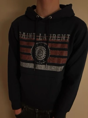 Saint Laurent hoodie XS – flagglogo - Saint Laurent hoodie i storlek XS Klassisk navyblå färg och clean passform som funkar perfekt till både jeans och kostymbyxor.  Tröjan är i mycket bra skick, helt utan defekter. Känns exklusiv och sitter riktigt bra på kroppen.  ⚜️ Märke: Saint Laurent ⚜️ Storlek: XS ⚜️ Färg: Svart ⚜️ Skick: Mycket bra skick, inga defekter ⚜️ Modellen på bilden är 177 cm och väger 57 kg  Mått (platt mätta): ⚜️ Midja till axel: 56 cm ⚜️ Axel till axel: 45 cm  Redo att skickas 📦