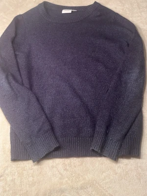 Mörkblå stickad tröja - Mysig mörkblå stickad tröja med rund halsringning och ribbade muddar vid ärmslut och nederkant. Perfekt för lager-på-lager och enkel att matcha med jeans eller kjol.