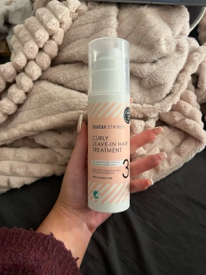 Matas Striber Curly Leave-In Treatment - Curly Leave-In Hair Treatment från Matas Striber i en smidig pumpflaska. Produkten är ljusrosa och vit med svarta detaljer och är speciellt framtagen för lockigt eller vågigt hår. Ger fukt, näring och skydd till håret utan att sköljas ur.