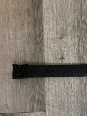 Svart monogram bälte  - Snyggt svart bälte med klassiskt. Bältet har ett diskret rutmönster och präglad logga på lädret. Perfekt accessoar för att lyfta din outfit med en lyxig touch.