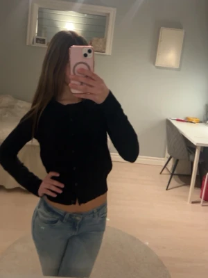 Svart cropped kofta med knappar - Snygg svart cropped kofta med knäppning framtill och långa ärmar. Perfekt att styla med jeans eller kjol för en trendig look. Enkel och stilren design som passar till många outfits.