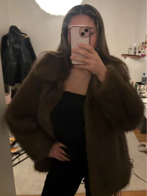 Brun pälsjacka med klassisk krage - Helt ny brun pälsjacka med klassisk krage och lång ärm. Jackan har en loose passform och är perfekt för att hålla dig varm under kyliga dagar. köpt för typ en månad sen och returrätten har gått ut därav säljer jag den🥲har inte hunnit använda den ens bara provat på och råkade dra av prislappen. 