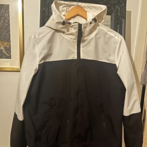 vind/regn jacka - passar dig som vill använda den ute och slit och släng! den har några fläckar som nog går bort i tvätten (fråga efter bilder). min hund har bitit på den (bild 5)  passar om du inte är rädd om jackan! den har en ficka på vardera sida och dragsko/resår runt luvan och mudden!