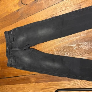 Replay Anbass svarta slim jeans 31 - Svarta Replay Anbass jeans i slim fit med klassisk femficksdesign och diskret tvättad look. Jeansen har snygga detaljer på bakfickan och är tillverkade i stretchigt denim för en bekväm passform. Perfekta för dig som gillar en smal siluett.