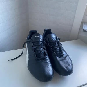 Puma King svarta fotbollsskor  - Säljer ett par klassiska Puma King fotbollsskor i svart skinn med vit Puma-logga på sidan och hälen. Skorna har snörning och dobbar för gräsplan. Perfekta för dig som vill ha stilrena och bekväma fotbollsskor med tidlös design. De är efterfrågad och unika. Storlek 44. Inga skador!