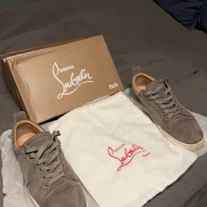 Grå sneakers från Christian Louboutin - Snygga grå sneakers i mocka från Christian Louboutin med den ikoniska röda sulan. Skorna har snörning och en stilren design som passar perfekt för en trendig look.