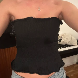 Svart bandeau tubtopp från XOXO friends - Säljer en svart bandeau tubtopp från XOXO friends. Toppen är smockad och har en lätt vågig kant upptill och nedtill. Den är ärmlös och sitter tight mot kroppen, perfekt till jeans eller kjol. Enkel och stilren design som är lätt att matcha.