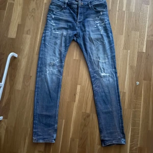 Blå slitna jeans från Jack & Jones - Snygga blå jeans från Jack & Jones med slitna detaljer och lätt tvättad look. Modellen är slim fit med klassisk femficksdesign och normal midja. Jeansen har dragkedjegylf och är tillverkade i bomull med lite stretch för skön passform. 30/30