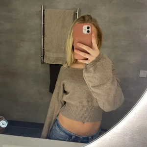 Beige croppad offshoulder stickad tröja - Säljer en beige croppad stickad tröja med offshoulder-modell och långa ärmar. Tröjan har bred ribbad mudd i midjan och vid ärmsluten, vilket ger en snygg och trendig passform. Perfekt för dig som gillar en chill och modern stil.