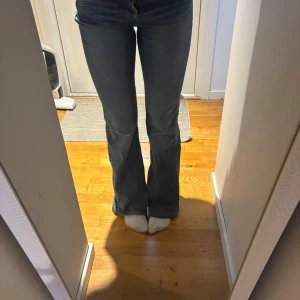 Blå bootcut jeans med hög midja - Snygga blå jeans med bootcut-modell och hög midja. Jeansen har klassisk femficksdesign och är tillverkade i ett mjukt denimtyg som sitter skönt. Perfekta för dig som gillar en tidlös look med lite utsvängda ben.