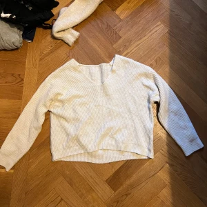 Ljus stickad v-ringad tröja - Mysig ljus stickad tröja med v-ringning och lång ärm. Tröjan har en avslappnad passform och är perfekt för lager-på-lager. Enkel och stilren design som funkar till många olika outfits.