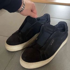 Svarta sneakers från Axel Arigato - Säljer ett par mörkblå sneakers från Axel Arigato med stilren design och vit platt sula. Skorna är i mocka, vilket ger dem en clean vibe. Bra skick!