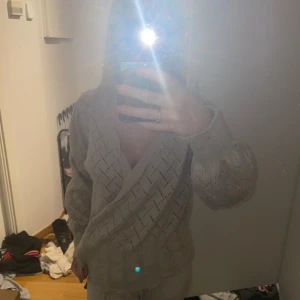 Beige omlottkofta med knytband - Säljer en beige stickad omlottkofta med knytband i midjan och snyggt hålmönster. Koftan har långa ärmar med lätt puff och ribbade kanter nertill. Perfekt för lager-på-lager och ger en chill men ändå söt vibe.