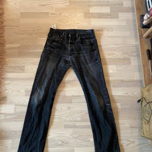 Levi's 501 svarta jeans W32 L36 - Svarta Levi's 501 jeans med klassisk rak passform och femficksdesign. Jeansen har en snygg tvättad look och är tillverkade i slitstarkt bomullsjeans. 