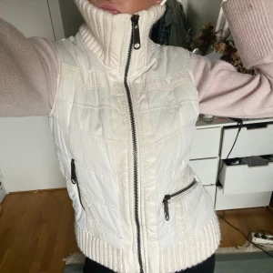 Vit väst med stickad krage - Snygg vit dunväst med bred, ribbstickad krage och nederkant. Västen har två dragkedjeförsedda fickor framtill och en markerad quiltad design. Det är två små fläckar på västens framsida men jag skulle inte säga att de märks när man har den på sig.
