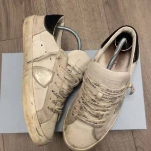 Philippe Model vita sneakers med text - Snygga vita sneakers från Philippe Model med handskriven text på snören och plös. Skorna har svarta detaljer vid hälen, rund tå och platt sula. Materialet är en mix av skinn och mocka, vilket ger en cool kontrast. Perfekt för dig som gillar unika och trendiga sneakers.box ingår ej