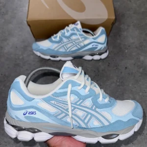 ASICS nyc skor - Fräscha ASICS Gel sneakers med snygg ljusblå och vit färgkombination. Skorna har mesh- och syntetpaneler, klassisk snörning och en chunky, stötdämpande sula med grå detaljer. Perfekt för dig som gillar sportig och modern stil.