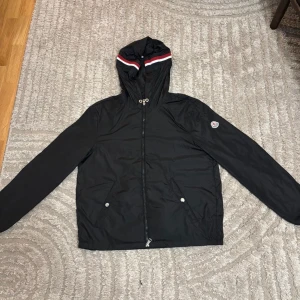 Moncler Grimpeurs - Säljer en Moncler Grimpeurs vindjacka i svart, storlek 3L. Jackan har använts sparsamt av min lillebror men är i nästan nyskick, inga märken, inga fläckar ser ut som ny. Han har helt enkelt växt ur den, den har blivit lite för liten i ärmar och midja, så därför får den gå vidare till någon som får mer användning av den.  En riktigt snygg och stilren vindjacka med huva lätt, vindtät och perfekt för både vår och höst.