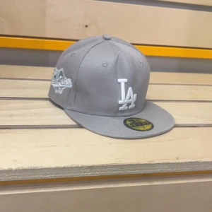 Grå LA-keps från New Era 59FIFTY - Snygg grå keps från New Era 59FIFTY med LA-logga i vitt framtill och broderad detalj på sidan. Helt ny, provat den 1 gång. Ända anledningen till att jag säljer den är pågrund av att den inte passar mig 