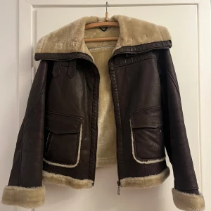 Brun fodrad läderjacka - Säljer en brun läderjacka med mjukt offwhite foder och krage. Jackan har två stora fickor framtill, dragkedja och snygga spänndetaljer på sidorna. Perfekt höst/vinter-jacka i mycket fint skick!🍁obs står ej storlek men skulle tro s-m!