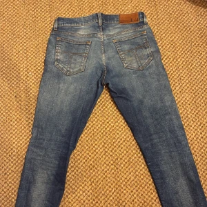 Blå tiger of sweden jeans - Snygga blå jeans från tiger of sweden med klassisk femficksdesign och tydliga slitningar. Jeansen har en slim passform, normal midja och detaljerade bakfickor med kontrastsömmar. Tillverkade i mjukt jeanstyg med stretch för extra komfort. Storlek 29/32. Jeansen har lite defekter här och där. En tråd som sitter lite löst i vänstra fickan. En fläck på högra bakfickan som är lite svår och få bort. Befintligt skick.